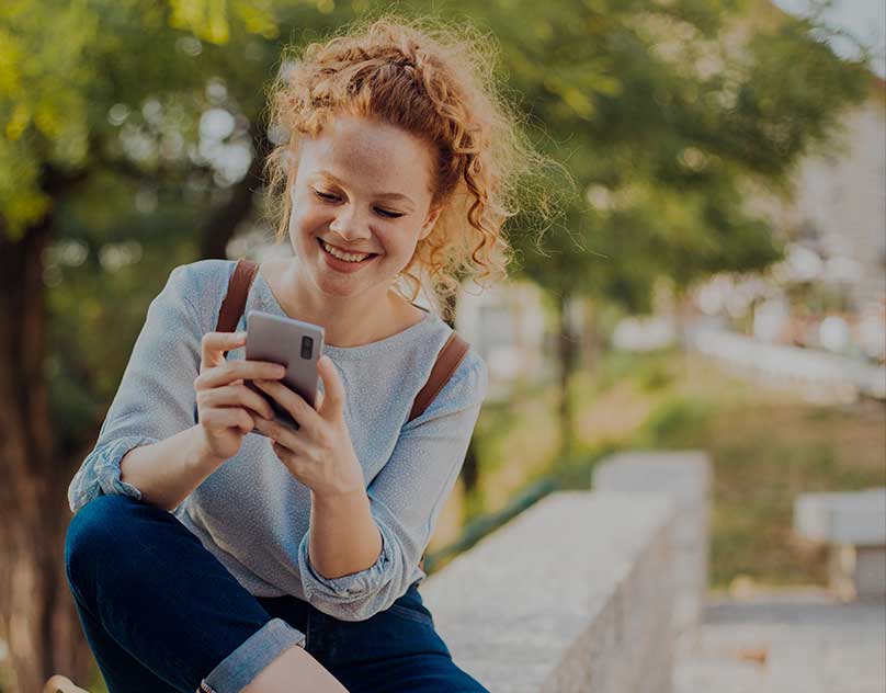 A young woman smiles as she looks at her smartphone.