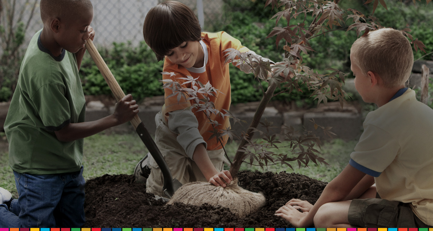 Three children are using teamwork to plant a young tree together. The Samsung Global Goals app allows everyone to participate in creating a brighter future. 